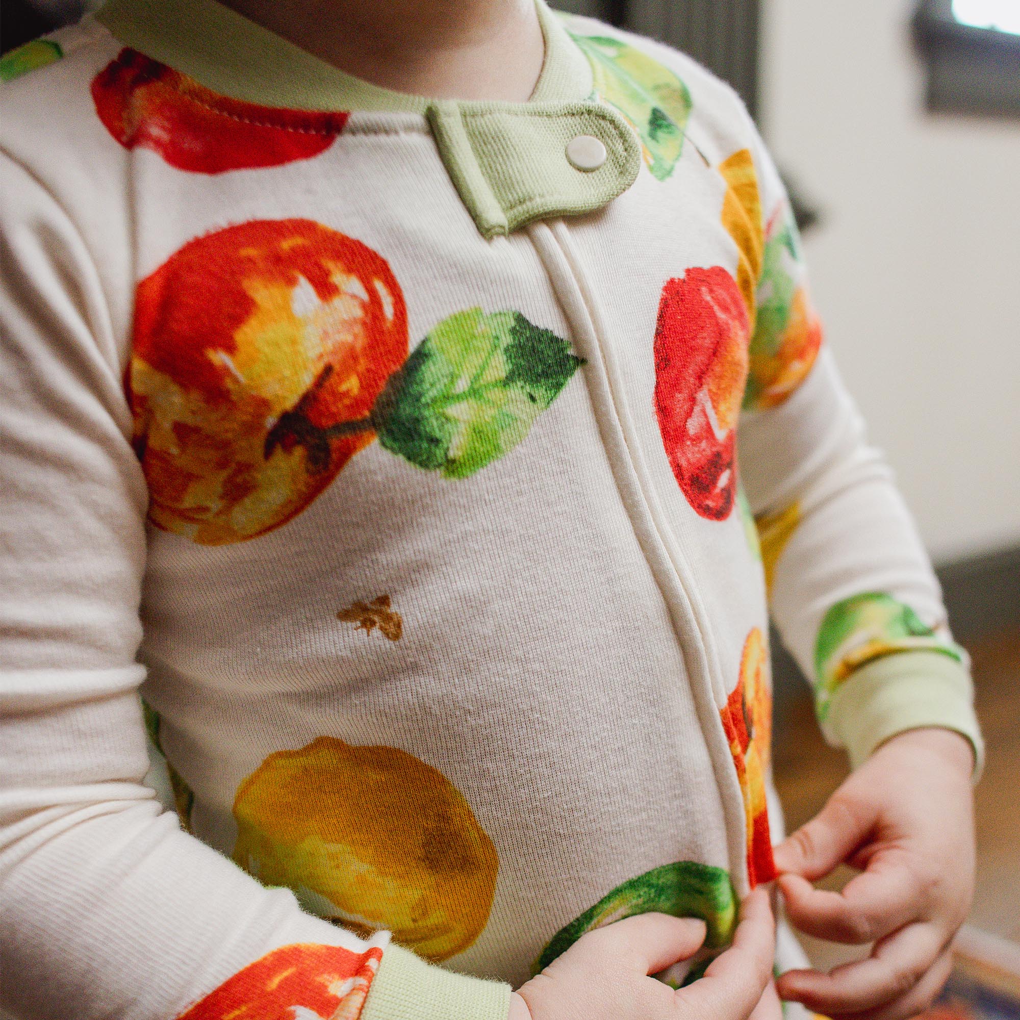 Child wearing a onesie with fruit patterns in a kitchen setting