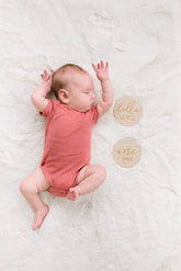 Newborn baby in a pink onesie lying on a white blanket with &