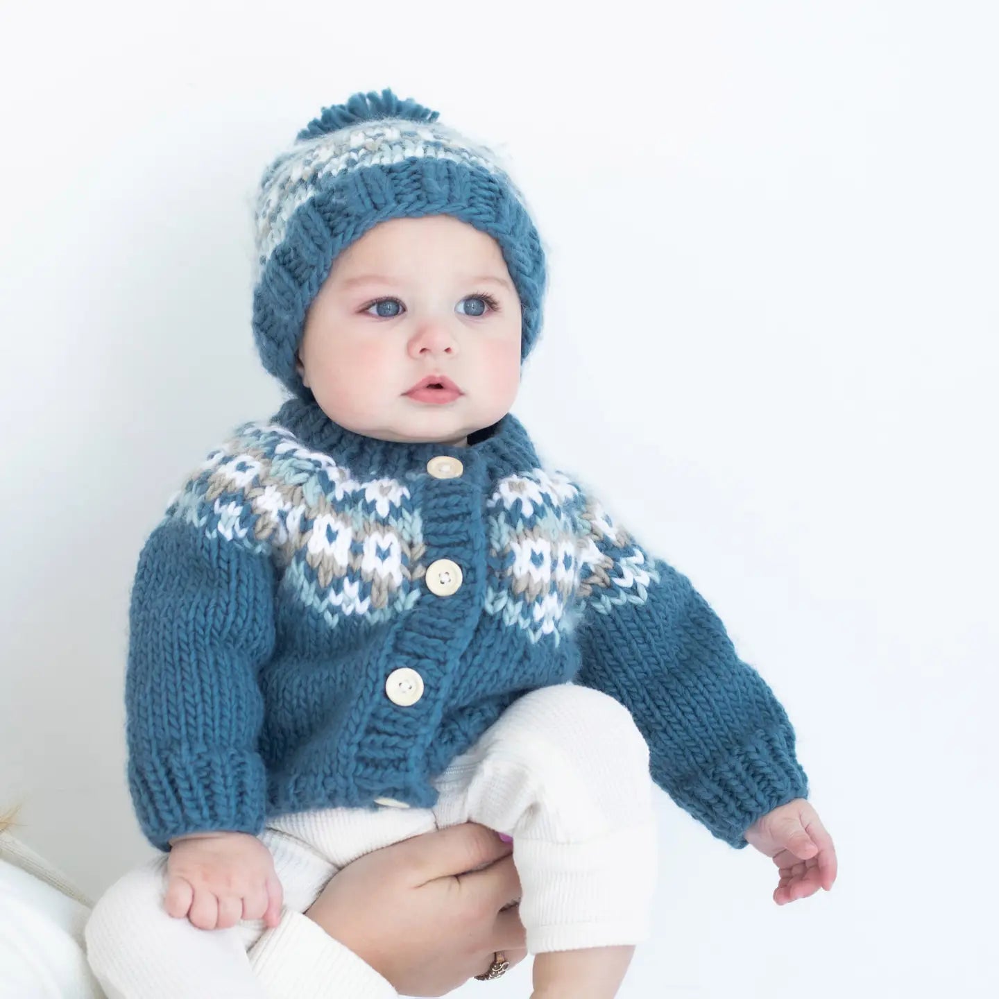 Baby wearing a blue knitted cardigan and hat on a white background