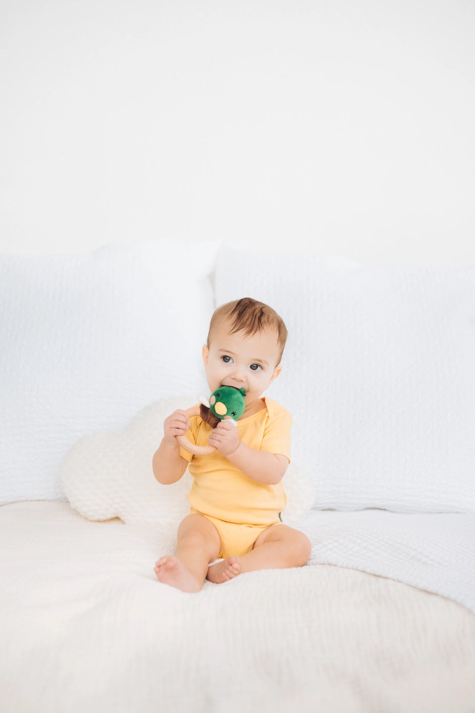 Baby sitting on a white surface holding a green toy