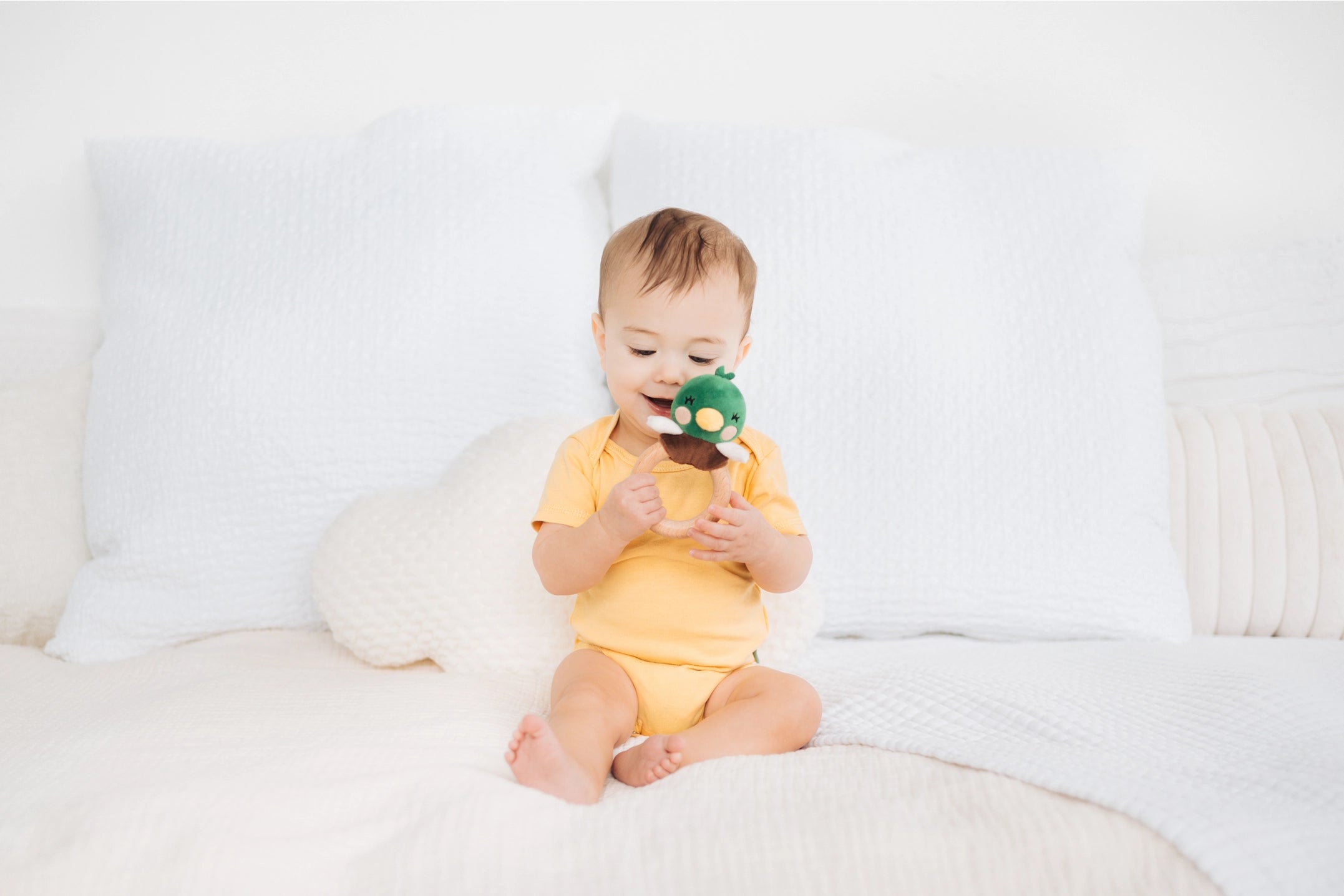 Baby sitting on a white couch holding a green toy