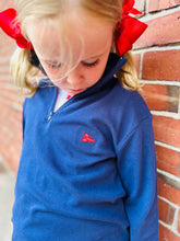 Child wearing a blue sweater with a lobster embroidery, standing against a brick wall.