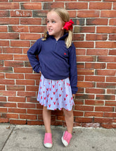 Young girl in a blue top and  lobster patterned skirt standing against a brick wall.