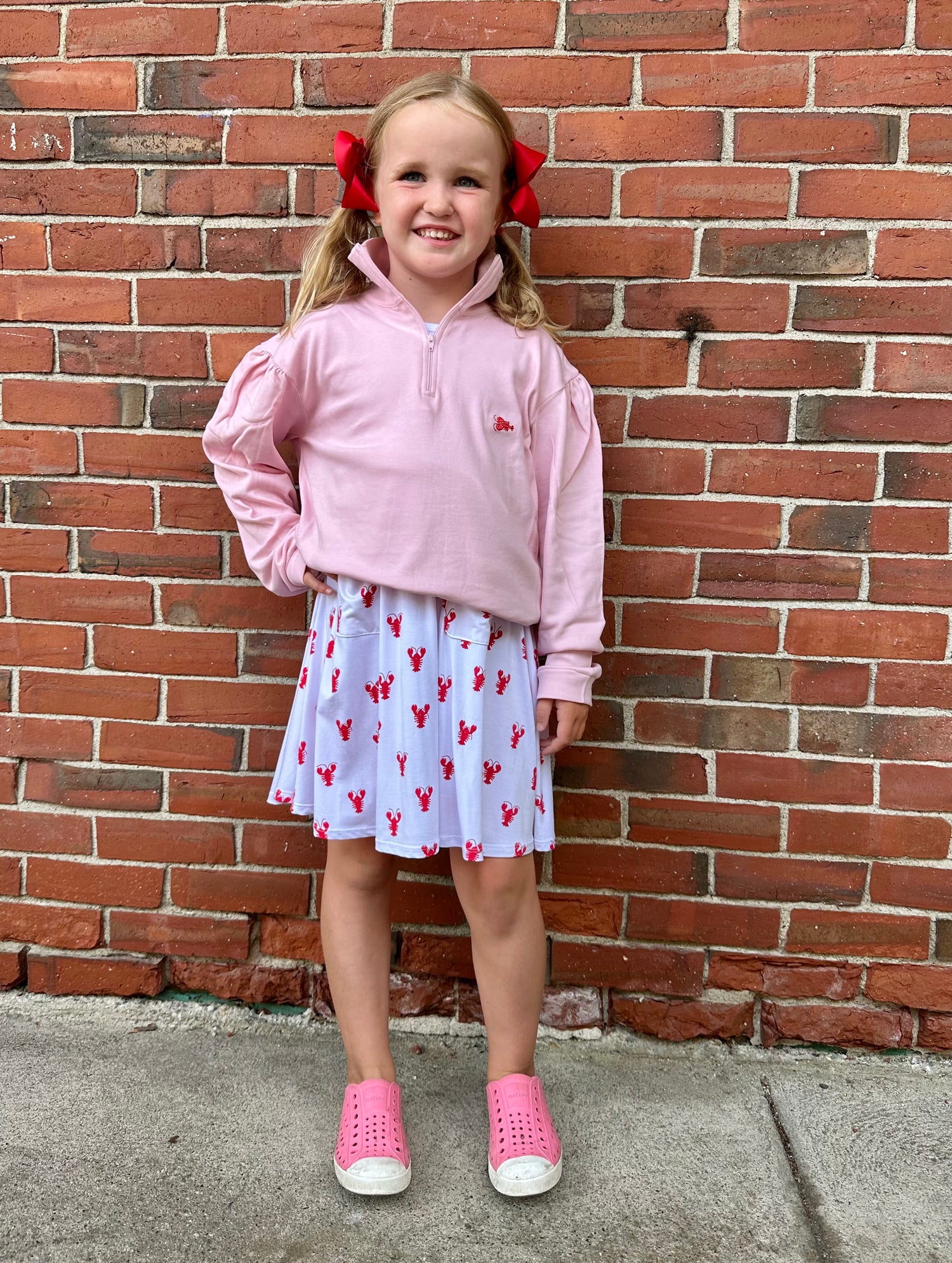 Young girl in pink outfit standing against a brick wall