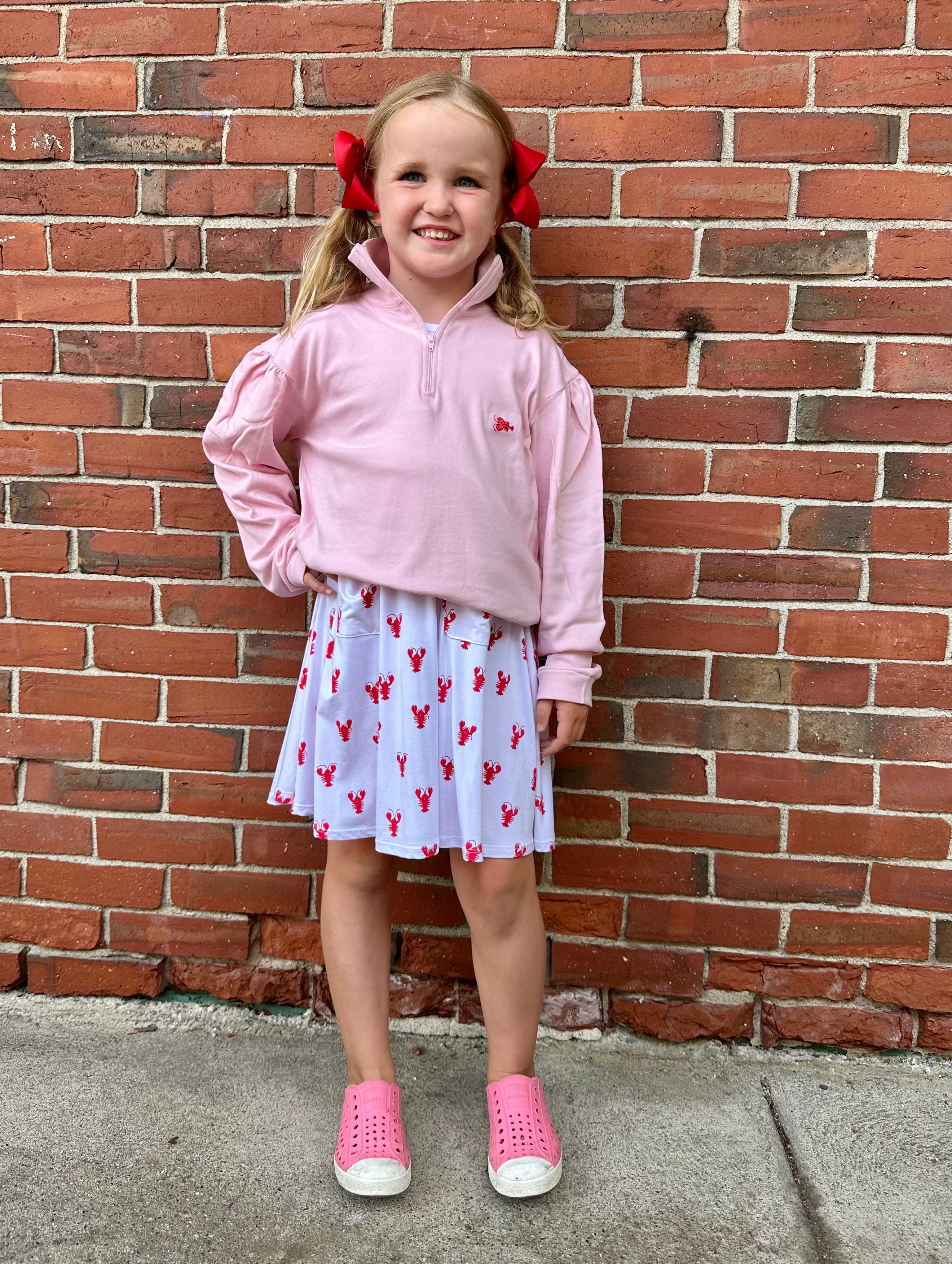 Young girl in pink outfit standing against a brick wall