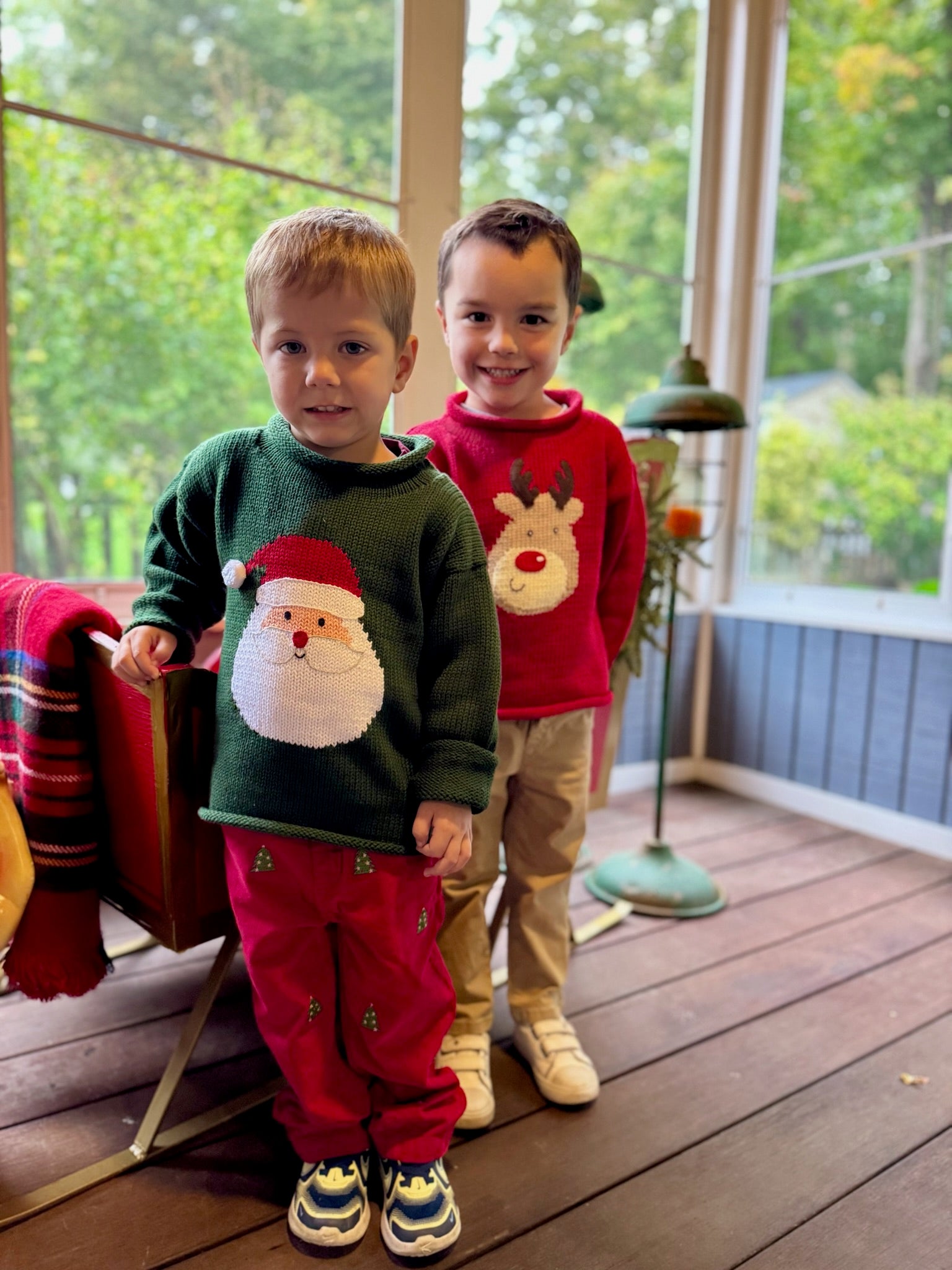 Two children wearing festive sweaters on a wooden deck.