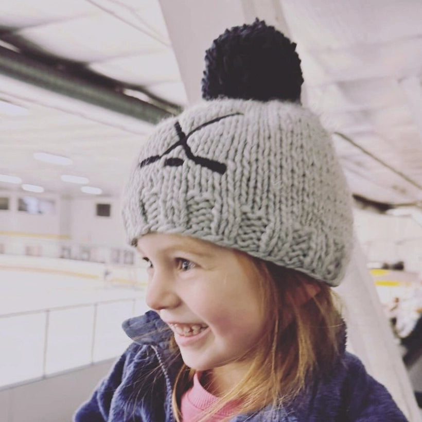 Child wearing a gray knit beanie with a black pom-pom indoors.