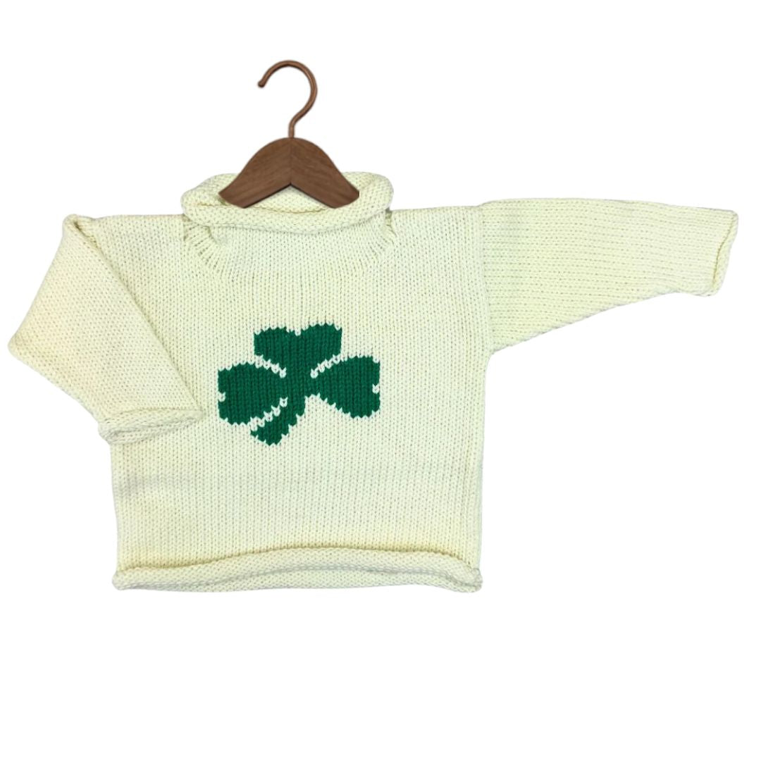 A cream-colored knit baby sweater with a green shamrock on the chest, displayed on a wooden hanger against a white background.