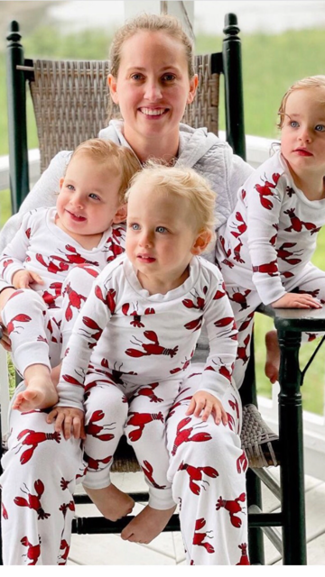 Three children and a woman wearing matching white long-sleeve pajamas with a red lobster print, posed together on a porch rocking chair.