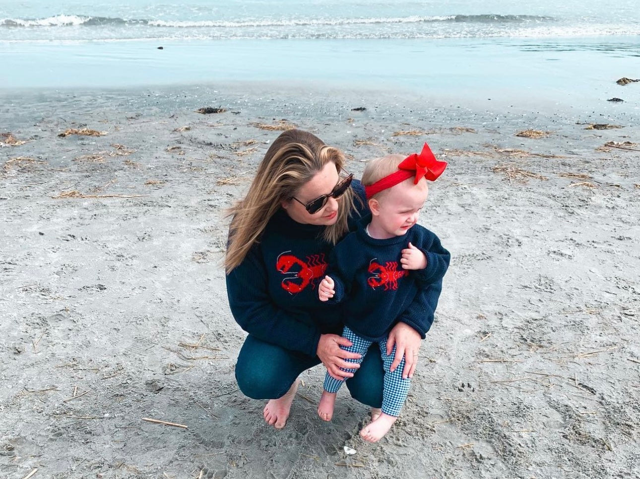 on the beach women is wearing navy lobster sweater and baby is wearing kids version of sweater