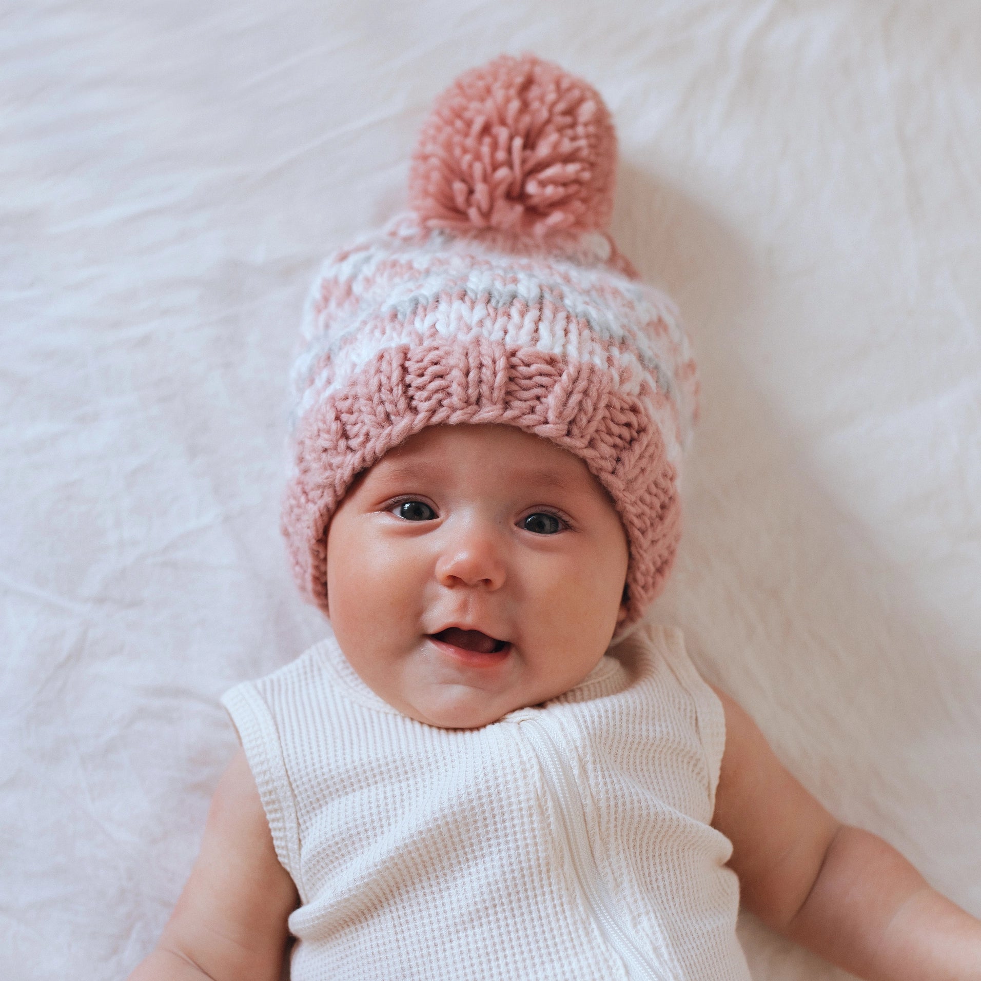 Baby wearing a pink knitted hat with a pom-pom on a white background