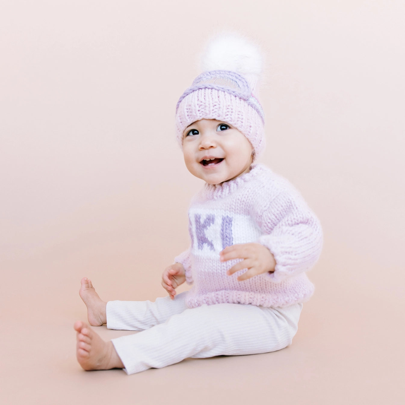 Baby wearing a pink knit sweater and hat with &