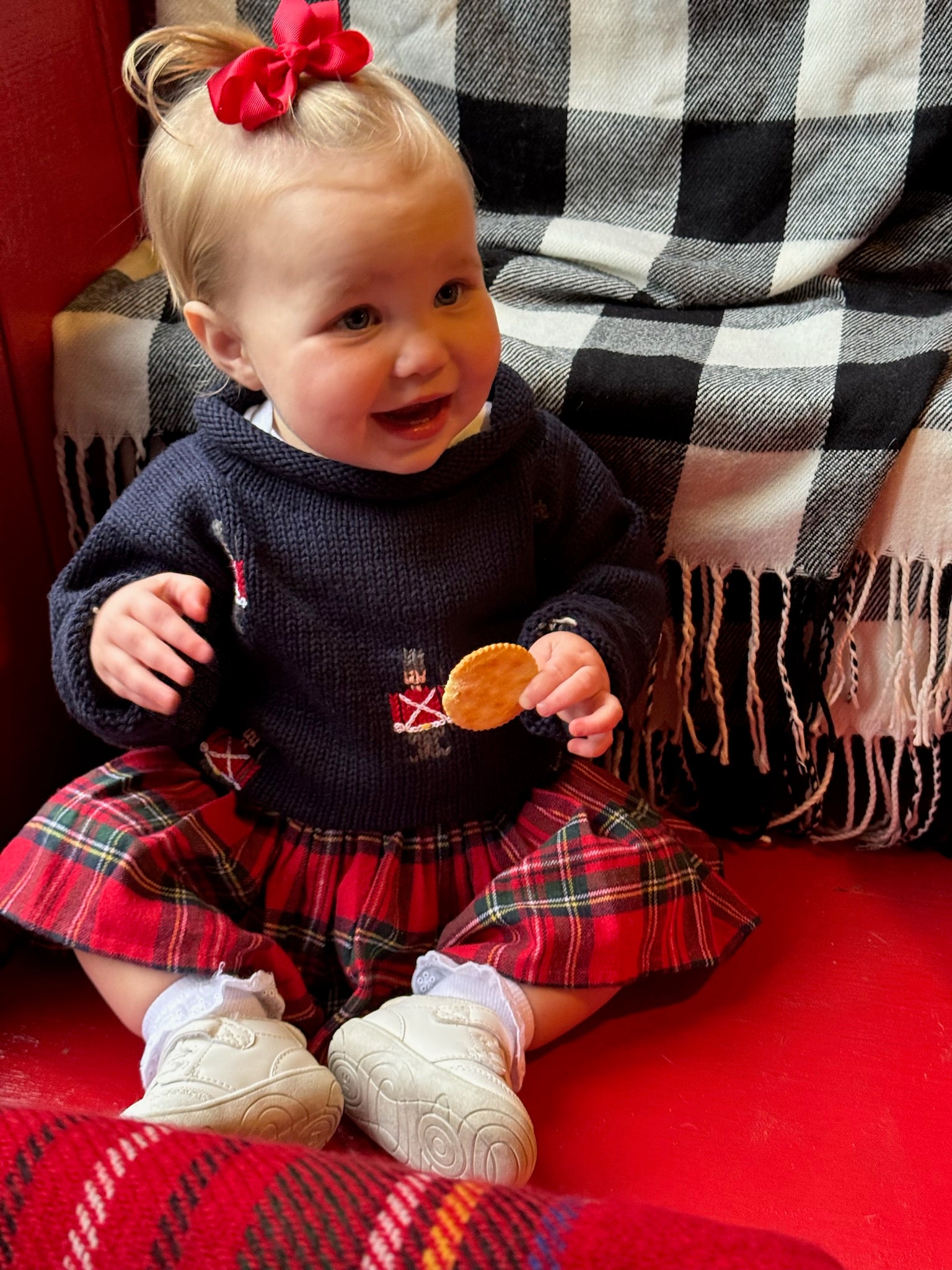 Child wearing a dark sweater with a red plaid skirt, sitting on a checkered surface.