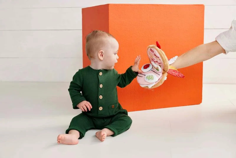 Baby in a green outfit playing with a toy in front of an orange box.