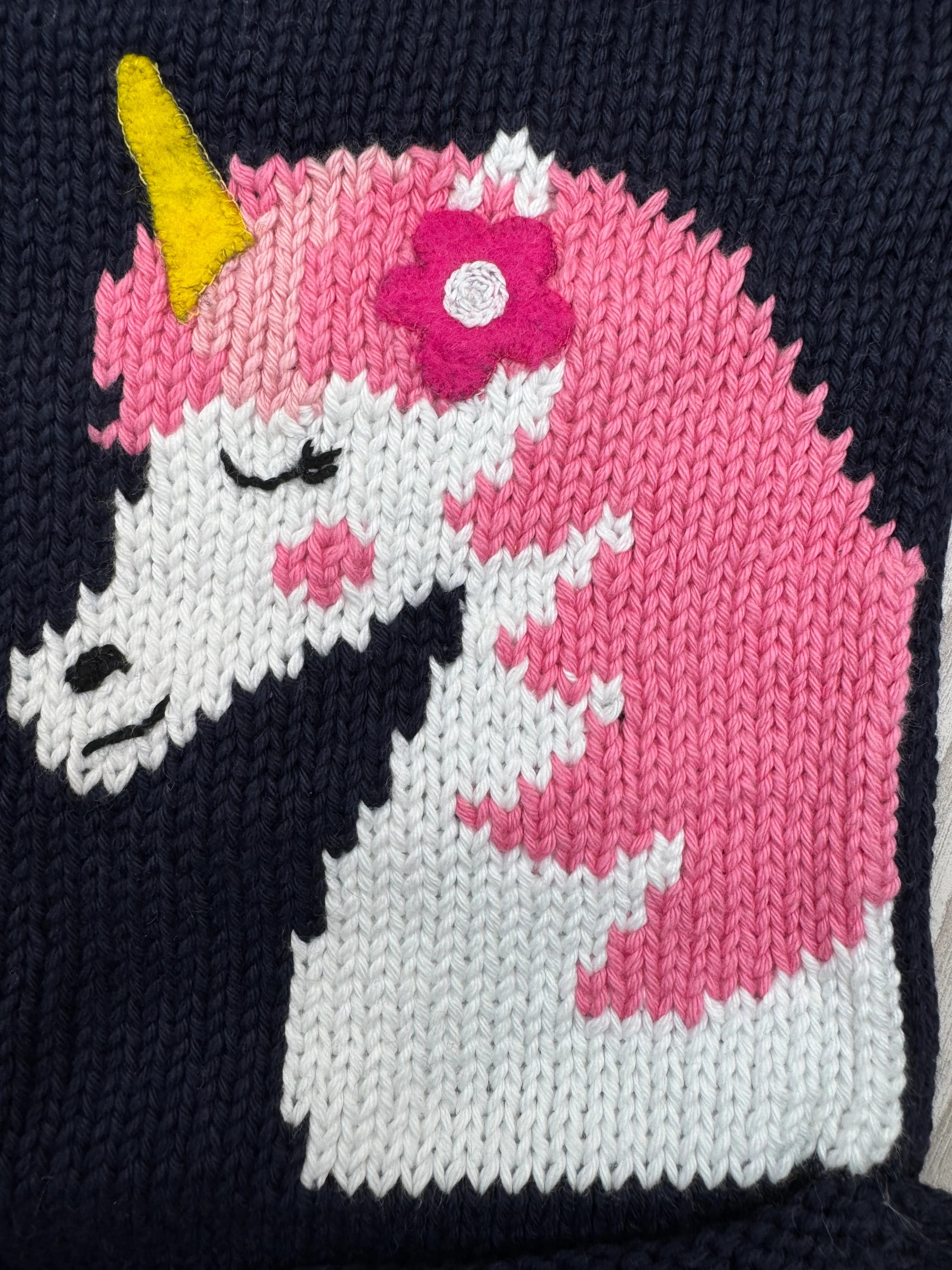 Knitted or crocheted design of a unicorn with pink mane and horn on a navy background