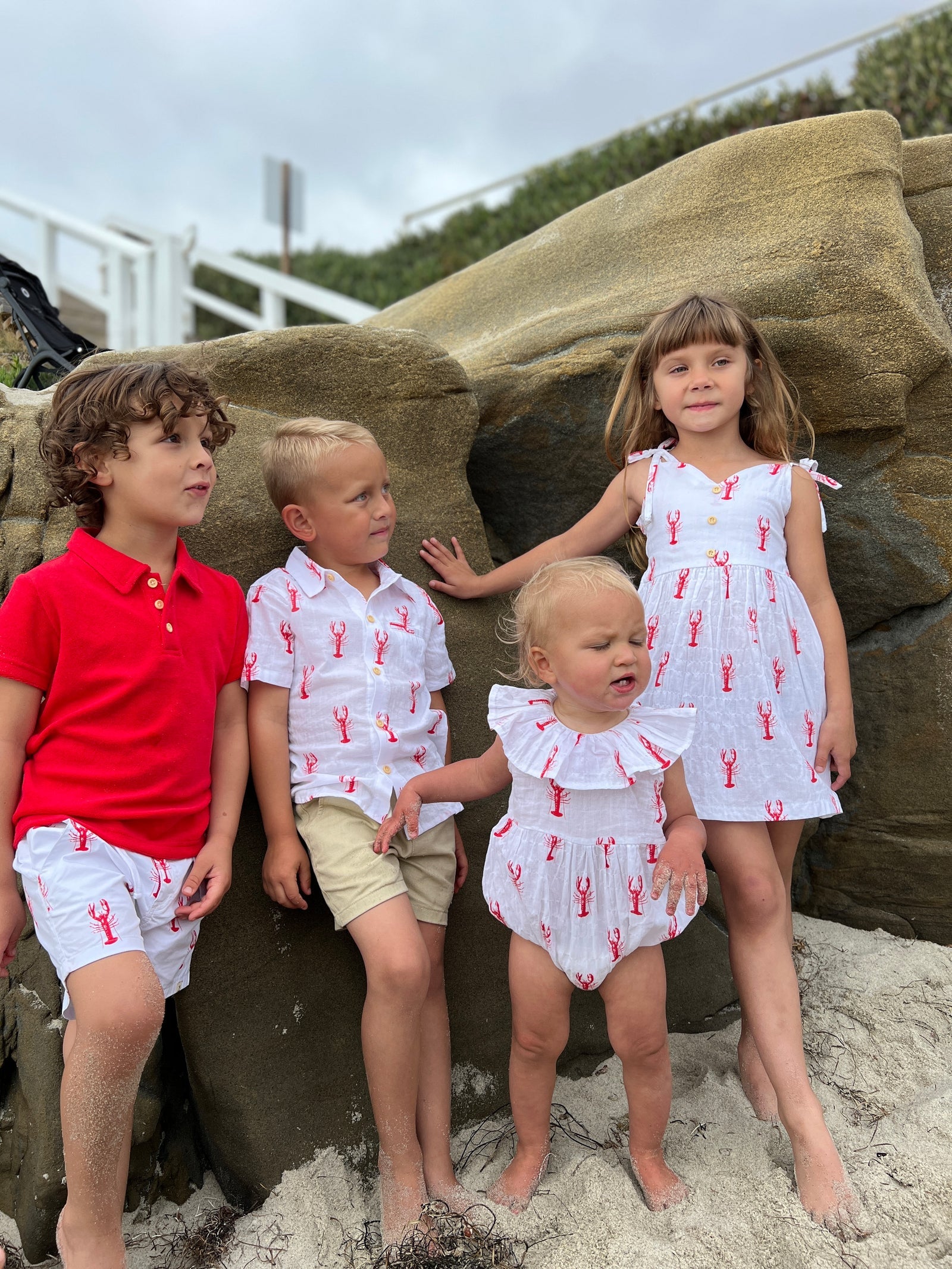 Four children in matching outfits standing on a sandy beach.