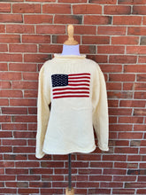 White sweater with American flag design on a brick wall background
