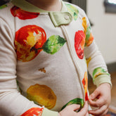 Child wearing a onesie with fruit patterns in a kitchen setting