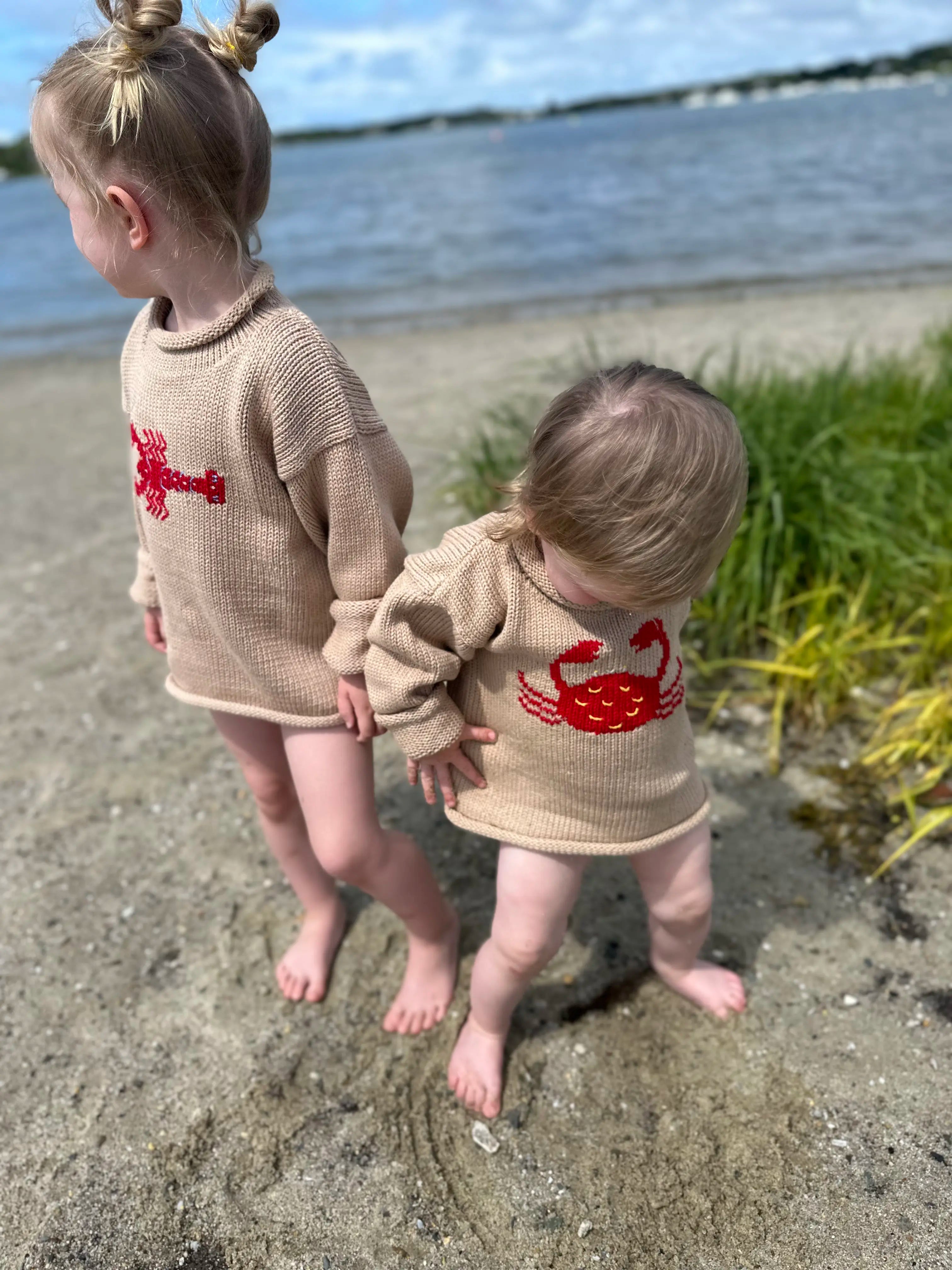 baby wearing tan crab sweater standing next to older sister wearing tan lobster sweater