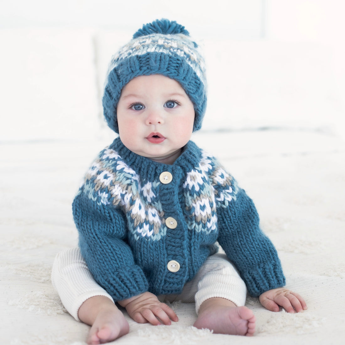 Baby wearing a blue knitted sweater and hat on a white background