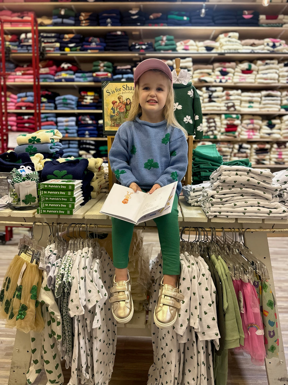 girl sitting on table with lots of shamrock clothing wearing a shamrock sweater and reading a book