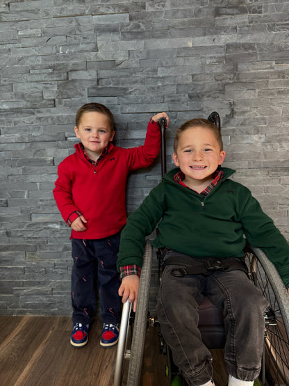 Two children, one standing and one in a wheelchair, against a gray stone wall.