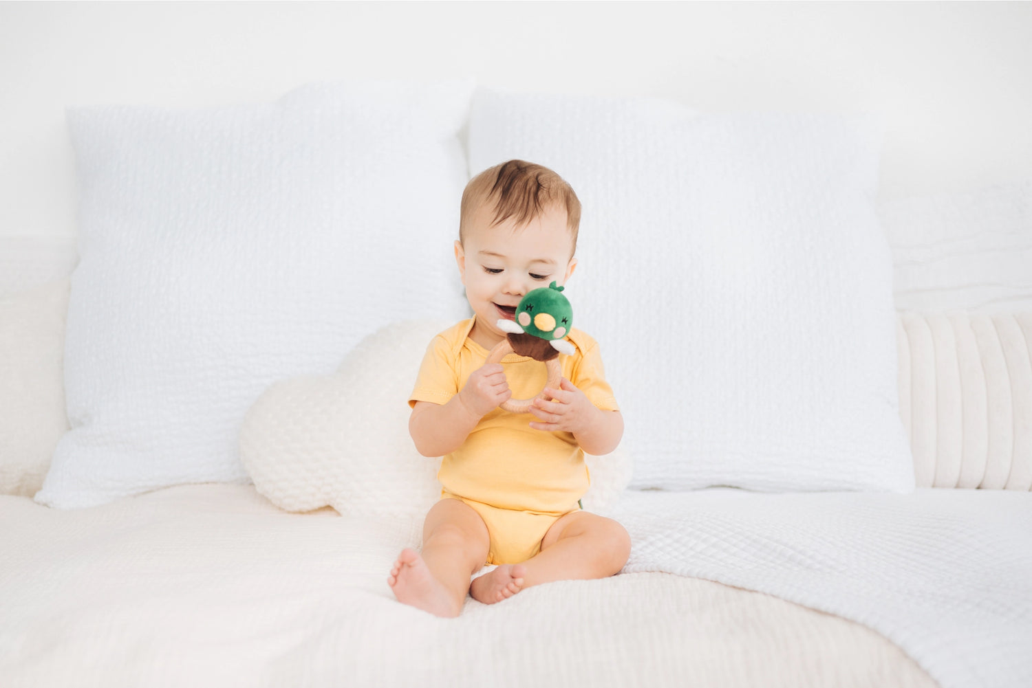 Baby sitting on a white couch holding a green toy
