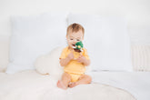 Baby sitting on a white couch holding a green toy