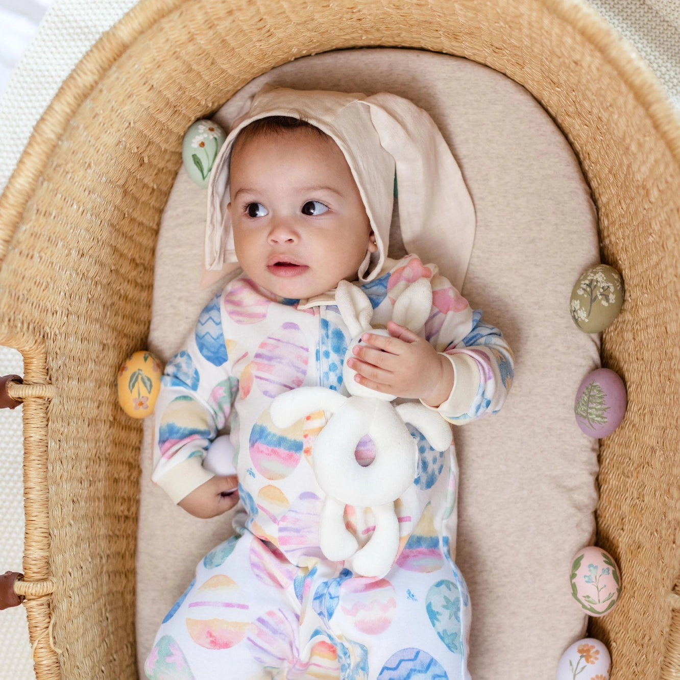 Baby in a Moses basket with colorful clothing and toys
