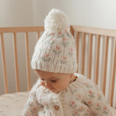 Baby wearing a knitted hat and sweater in a crib