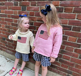 Two young girls wearing sweaters with American flag designs against a brick wall.
