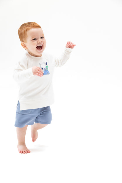 Child wearing a white long-sleeve shirt with a graphic and blue shorts on a white background
