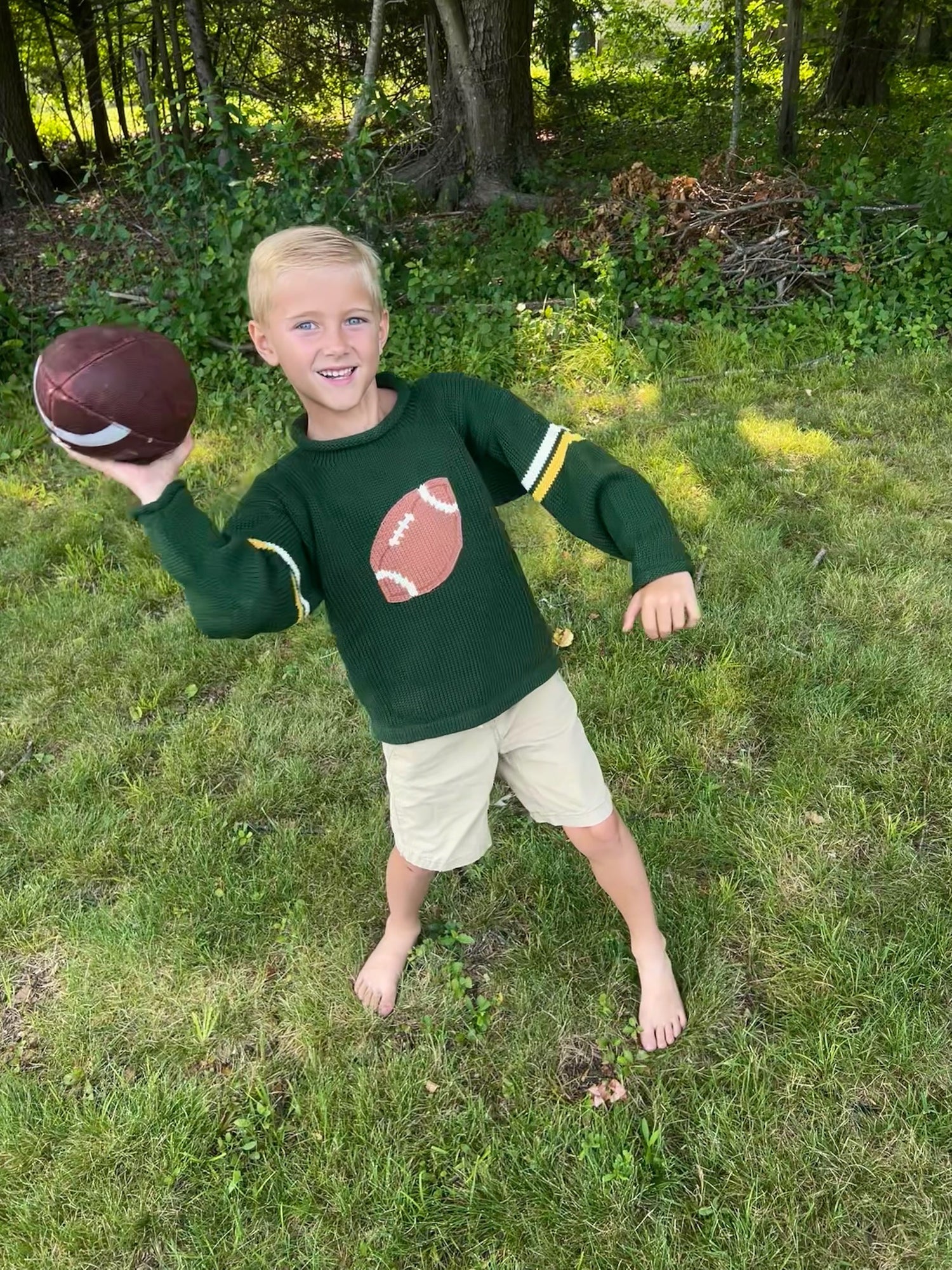 Child holding a football outdoors in a grassy area with trees in the background