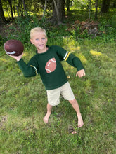 Child holding a football outdoors in a grassy area with trees in the background