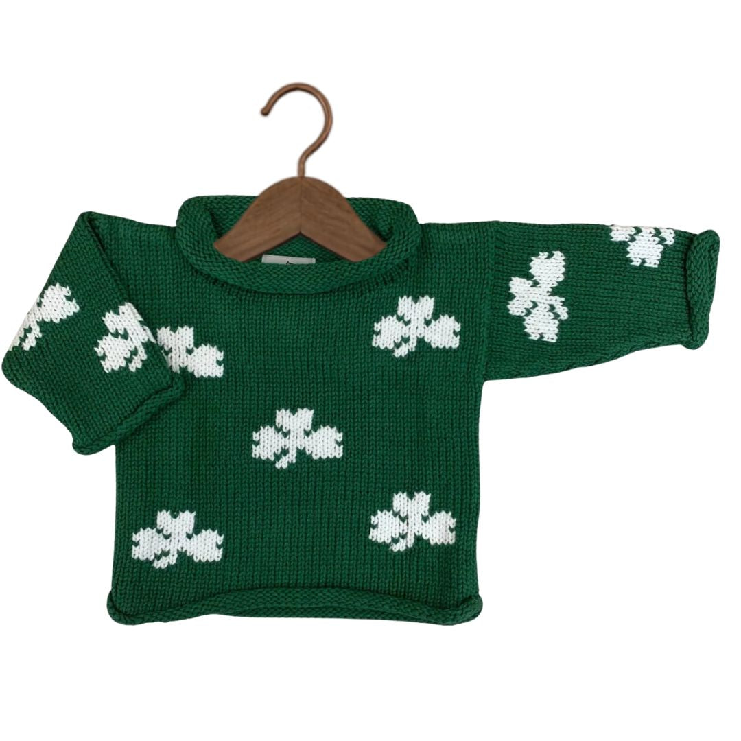A green knit sweater with white shamrock patterns, displayed on a wooden hanger against a plain white background.