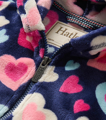 Close-up of a fleece zip-up hoodie with a navy blue base and a heart pattern in pink, white, and light blue. The brand name &