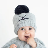 Baby wearing a gray knit hat with a black pom-pom on a white background