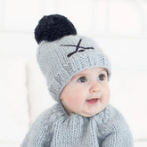 Baby wearing a gray knit hat with a black pom-pom and matching sweater on a white background