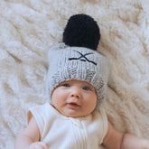 Baby wearing a knitted hat with a pom-pom on a soft, light-colored surface