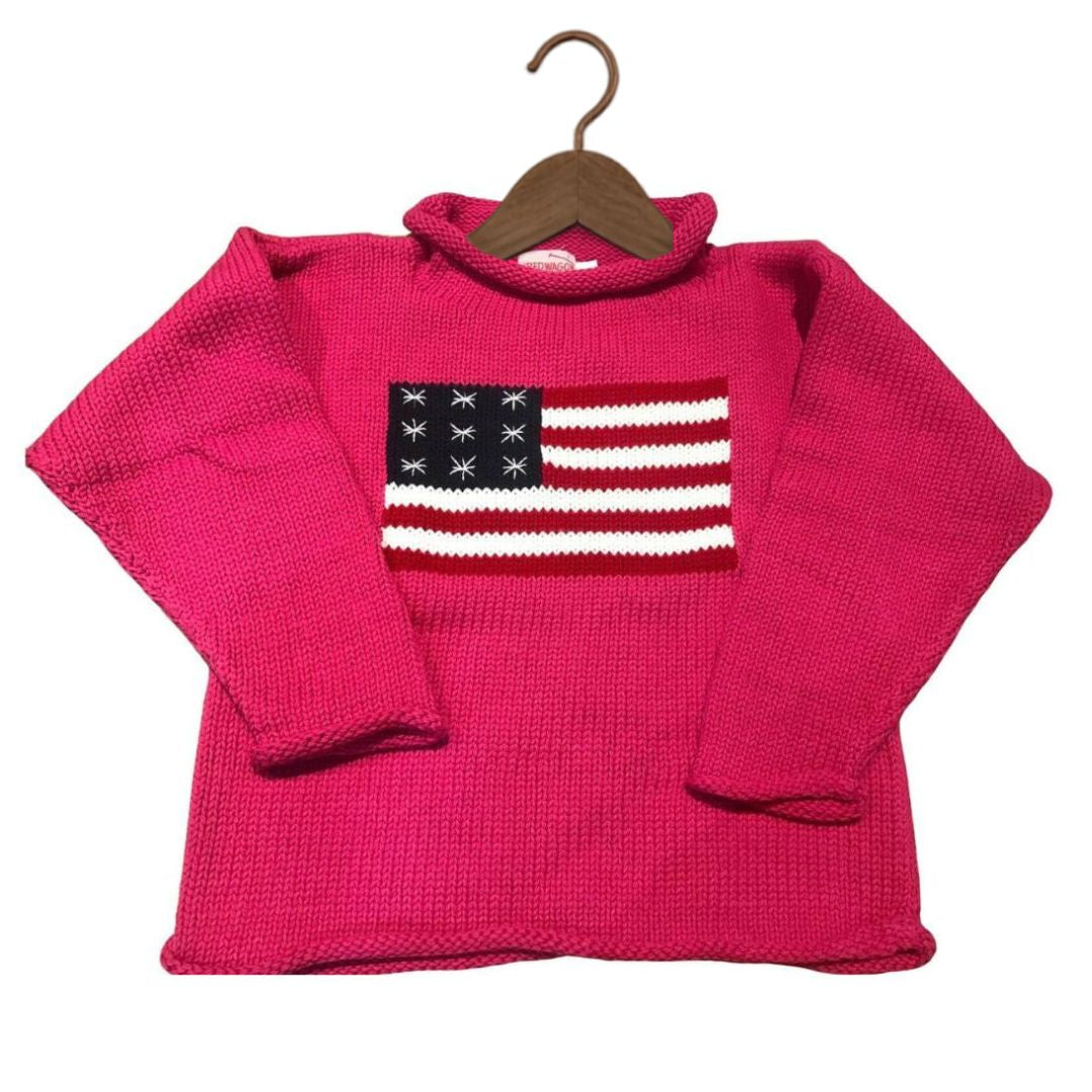 A bright pink knit sweater with a knitted American flag design on the chest, hanging on a wooden hanger against a plain white background.