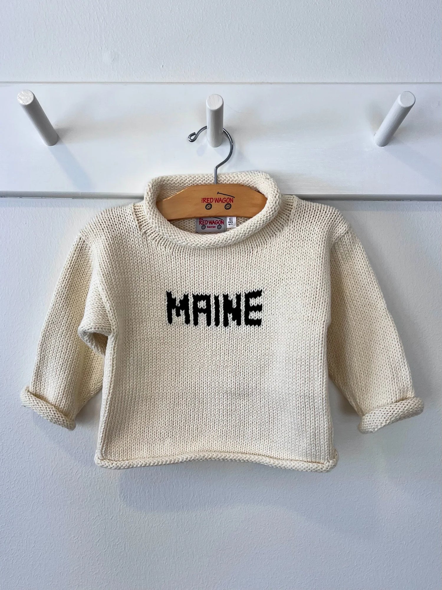 ivory sweater with hunter green Maine hanging on a peg rack