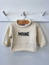 ivory sweater with hunter green Maine hanging on a peg rack