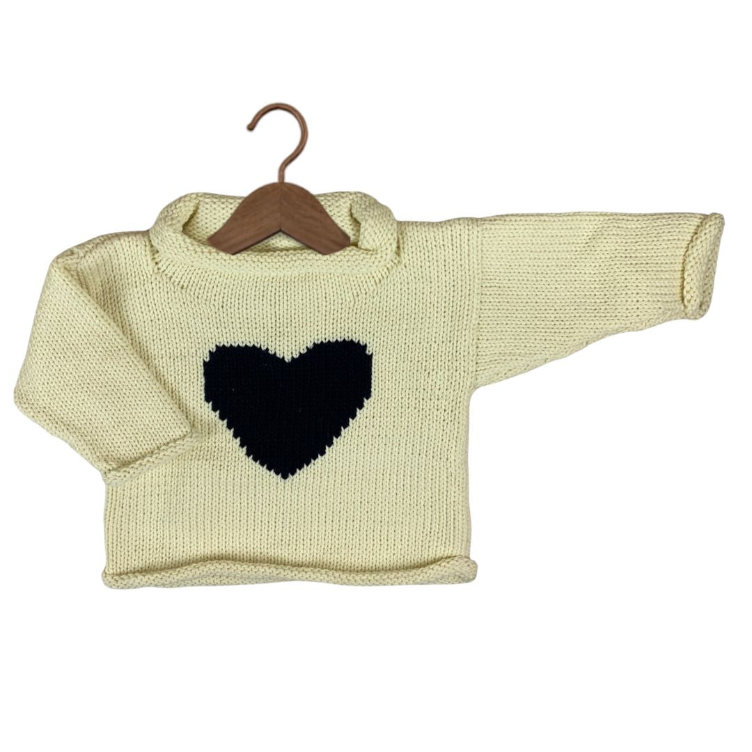 A cream-colored knit sweater with a black heart on the chest, displayed on a wooden hanger against a plain white background.
