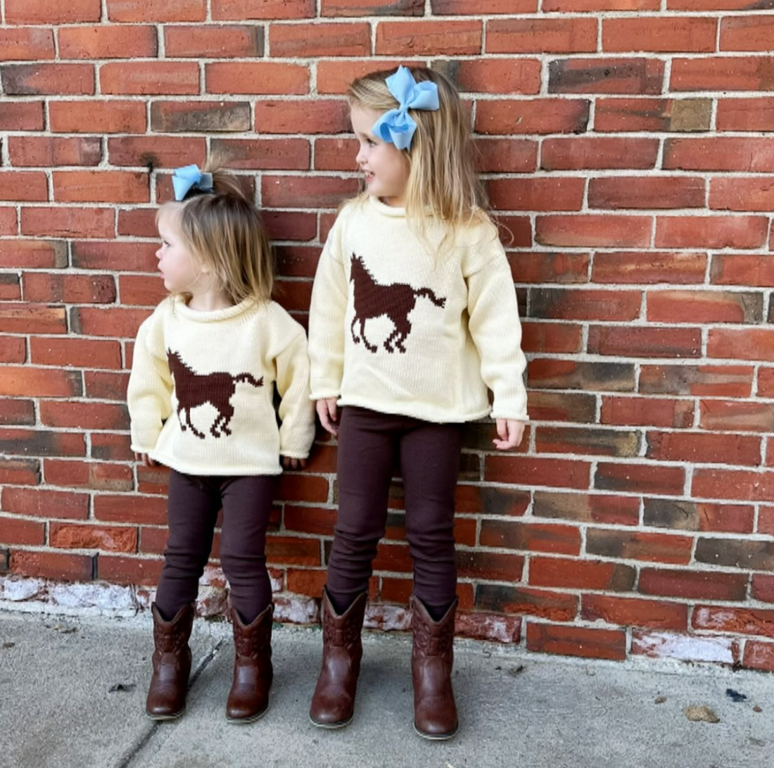 Two children wearing matching outfits with horse graphics against a brick wall.