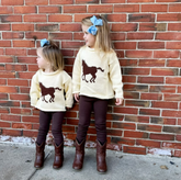 Two children wearing matching outfits with horse graphics against a brick wall.