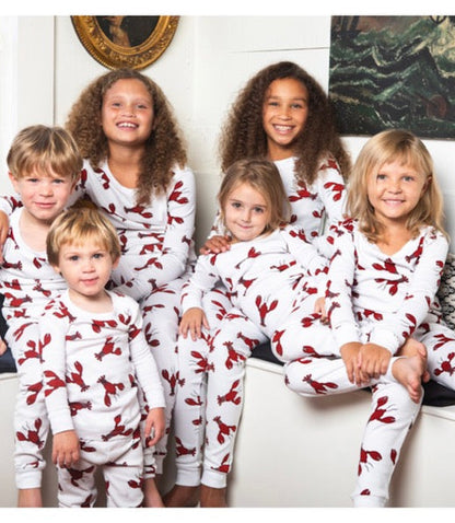 Six children wearing matching white long-sleeve pajamas with a red lobster print, posed together indoors. 