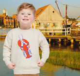 Child wearing a sweater with a lobster design in front of a waterfront scene with buildings and a dock.