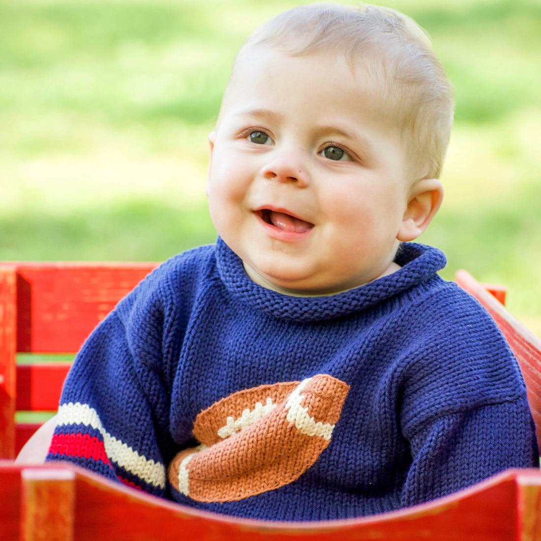 Child wearing a blue sweater with a football design, sitting outdoors.