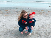 on the beach women is wearing navy lobster sweater and baby is wearing kids version of sweater