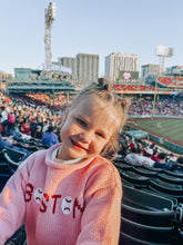 A young girl smiling in a pink knit sweater with &